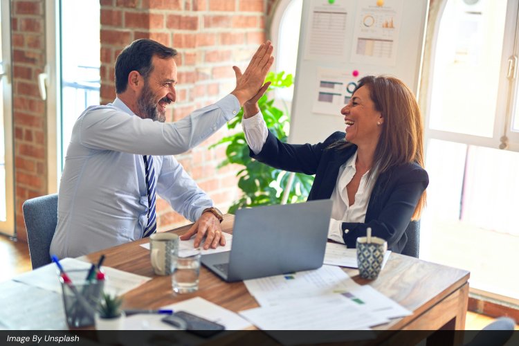 Two business professionals high-fiving in a modern office after successfully reaching a milestone in their digital marketing roadmap.
