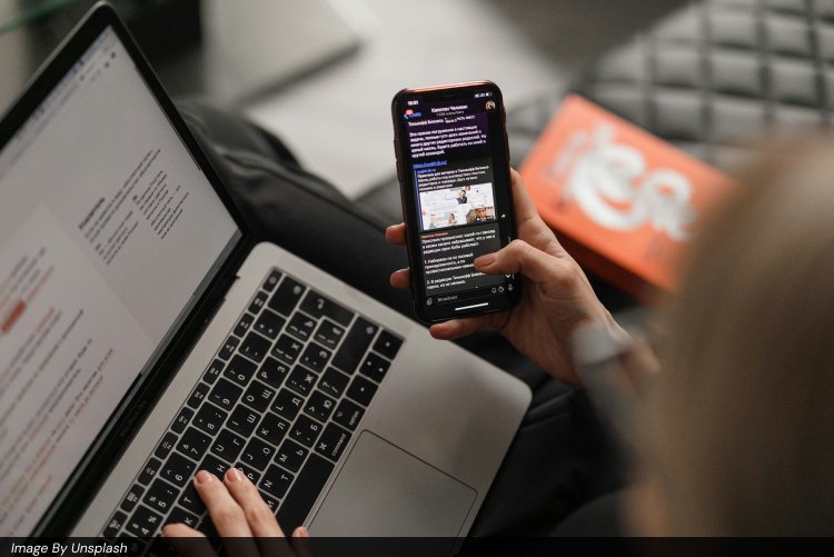 Person multitasking on a MacBook Pro laptop and smartphone, reviewing social media content, chat messages, and digital marketing materials on both devices, symbolizing modern PPC advertising, Facebook Ads and Google Ads management, content marketing, and full-funnel digital marketing strategies for business growth.