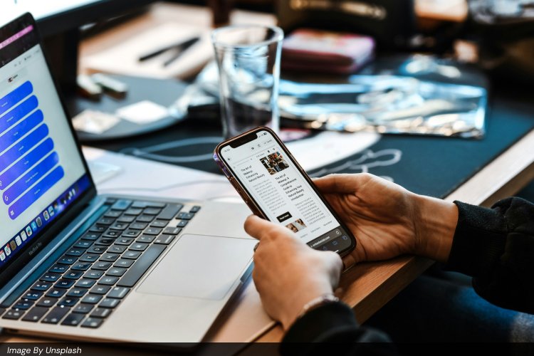 Close-up of hands holding a smartphone showing a digital content feed while a laptop screen displays a social media management dashboard with Instagram, Facebook, and TikTok icons, illustrating multi-platform digital marketing, Facebook Ads vs Google Ads comparison, PPC campaign management, and social media advertising tools used by marketers.