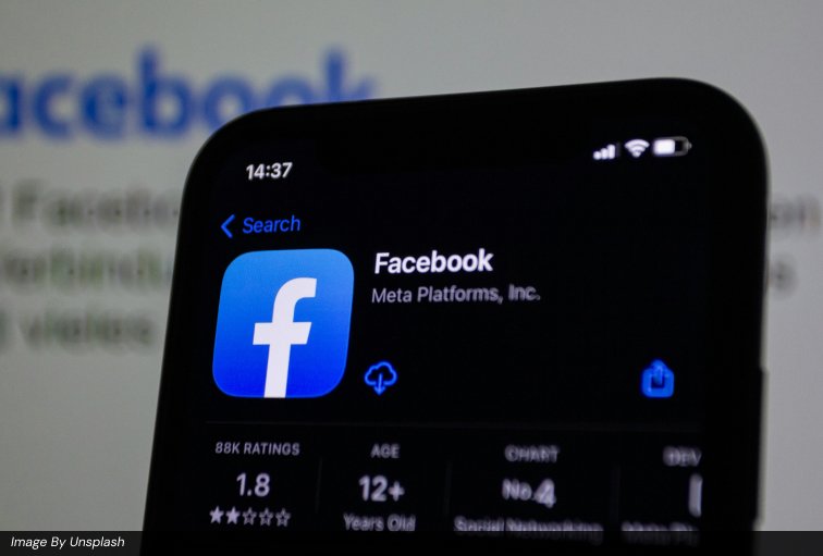 Smartphone displaying the official Facebook app by Meta Platforms Inc. with the blue Facebook logo, app store ratings, and age rating, set against a blurred background showing the Facebook website, representing Facebook Ads, Meta Ads, social media advertising, and paid social campaigns for digital marketing and lead generation strategies.