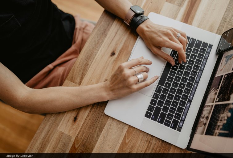 Overhead view of hands typing on a laptop keyboard at a wooden desk; representing as the featured image for Ai automation