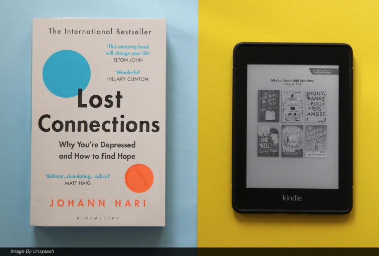 Physical paperback book next to a Kindle e-reader displaying Kindle Unlimited titles